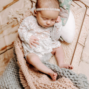 Baby in einem Bettchen mit Haarband in Kuscheldecken