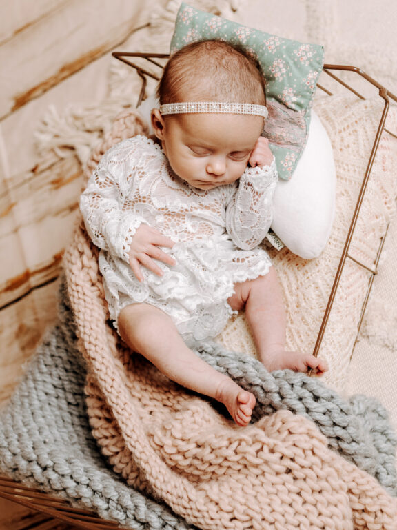 Baby in einem Bettchen mit Haarband in Kuscheldecken